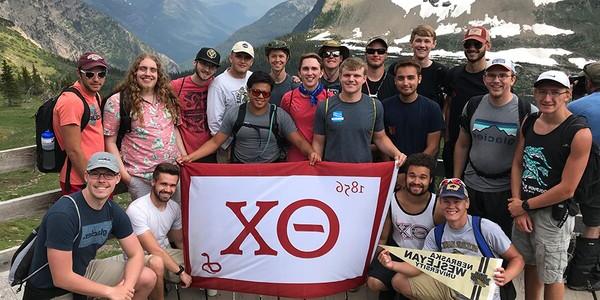 Several Theta Chi members holding banner in front of a glacier.