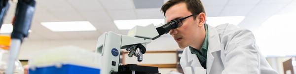 穿着实验室大褂的男学生正在通过显微镜观察.